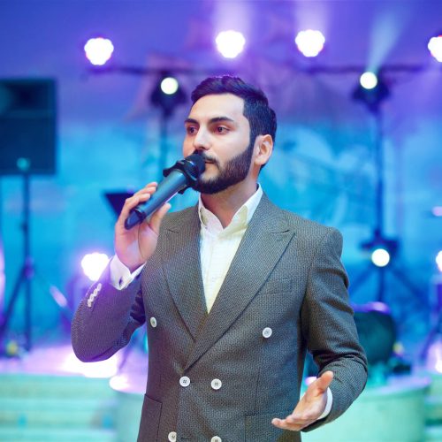 Charming young man leading acts at the evening concert in a gray suit under the light of the spotlights