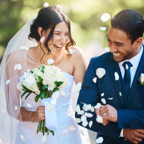 Love, wedding and couple walking with petals and guests throwing in celebration of romance. Happy, smile and young bride with bouquet and groom with crowd celebrating at the outdoor marriage ceremony.